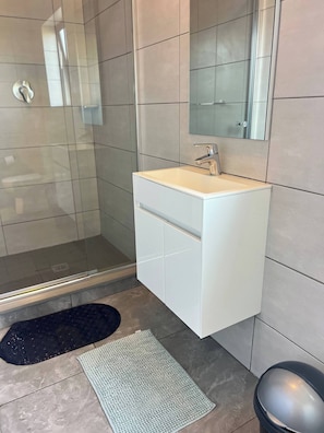 A modern bathroom with a glass shower enclosure, a white vanity with a mirror, and a black and white rug on the floor. - Luxury Apartment Overlooking the River (Midrand)