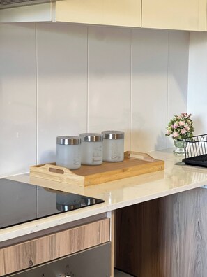 Una cucina con un piano di lavoro bianco, tre contenitori in acciaio inossidabile, un tagliere in legno, un tablet nero e una piccola pianta in vaso.
