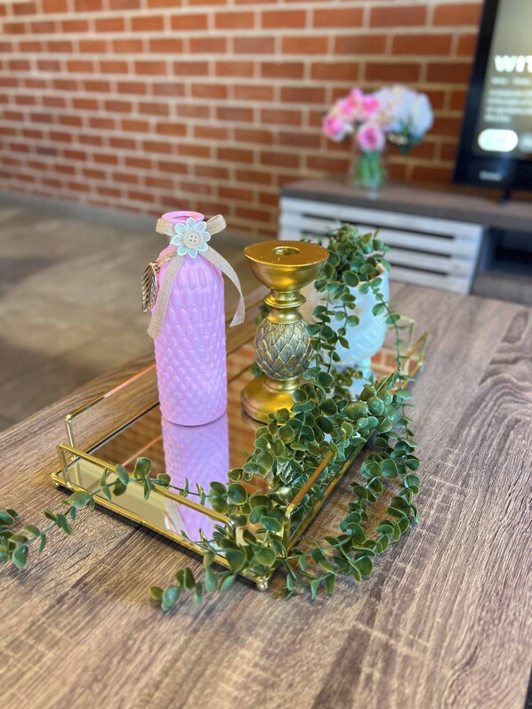 A wooden table with a decorative tray, a pink textured object, a golden candle holder, and green foliage. - Luxury Apartment Overlooking the River (Midrand)