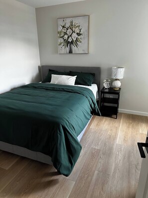 Un dormitorio con cama, una mesita de noche con lámpara, un reloj de pared y una obra de arte enmarcada.