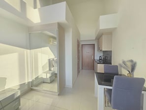 Un apartamento moderno con puerta de vidrio que da a un dormitorio, una kitchenette con estufa y un comedor con una silla y mesa.