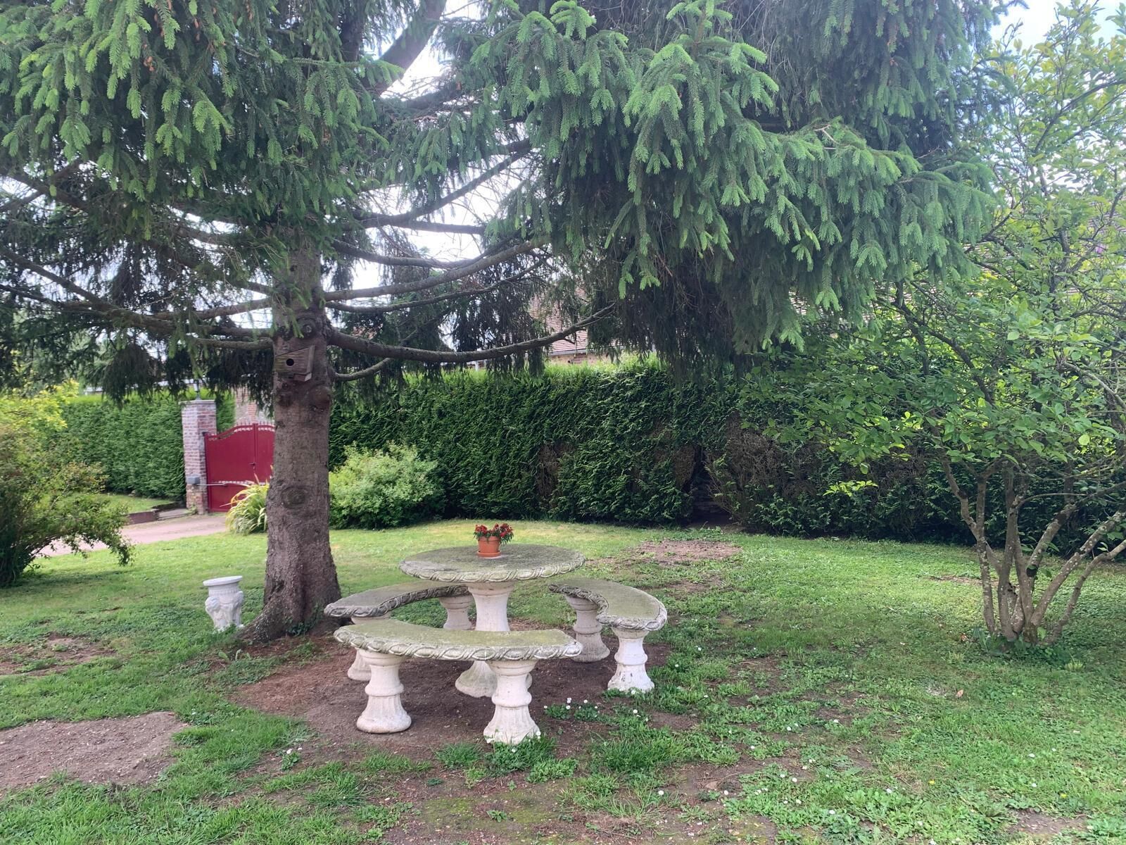 A garden with a stone table and benches, surrounded by greenery and a red gate.