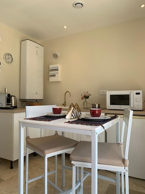 A small kitchen with a white table, two chairs, a microwave, a kettle, and a clock on the wall. - La Clérynette awaits you in the heart of Château de Gaillard (Les Andelys)