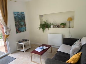 A living room with a sofa, a coffee table, a radiator, a bookshelf, and a painting. - La Clérynette awaits you in the heart of Château de Gaillard (Les Andelys)
