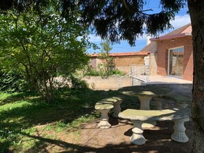 Un patio con un banco de piedra, un árbol y un edificio de ladrillo con techo rojo.