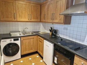 A kitchen with wooden cabinets, a washing machine, a dishwasher, a stove, and a sink. - Bright 2 BDR APT on Charlotte Quay Dublin (Dublin)