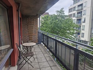 A balcony with a table and chairs, a brick wall, and a view of a tree and buildings. - Bright 2 BDR APT on Charlotte Quay Dublin (Dublin)