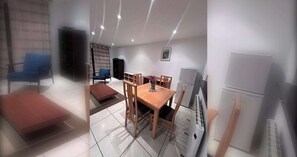 Ein modernes Wohnzimmer mit Essbereich, einem blauen Sessel, einem Holztisch und einem weißen Kühlschrank.