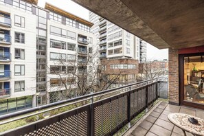 Een balkon met uitzicht op hoge wooneenheden, een metalen hek en een kleine tafel met een stoel.