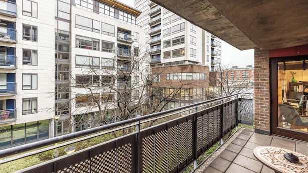 A balcony with a metal railing, a small table, and a view of high-rise buildings. - Bright 2 BDR APT on Charlotte Quay Dublin (Dublin)
