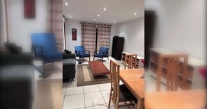 Ein Wohnzimmer mit einer Couch, zwei blauen Sesseln, einem Holztisch, einem Fernseher und einem Bücherregal.