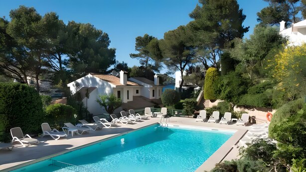 A swimming pool with lounge chairs, surrounded by trees and a building. - Beautiful House with Wi-Fi, Air Conditioning, and Pool in Exclusive Community (Cala de Sant Vicenç)
