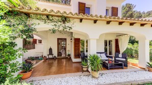 A villa with a covered patio, outdoor seating, and potted plants. - Beautiful House with Wi-Fi, Air Conditioning, and Pool in Exclusive Community (Cala de Sant Vicenç)