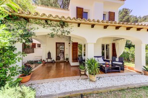 Een villa met een overdekt terras, buitenmeubels en potplanten.
