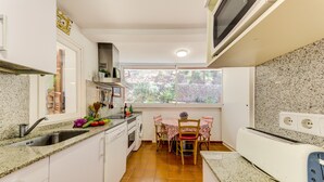 A compact kitchen with a sink, stove, and a dining area with chairs and a table. - Beautiful House with Wi-Fi, Air Conditioning, and Pool in Exclusive Community (Cala de Sant Vicenç)