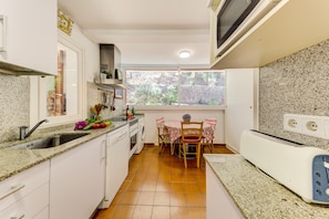 A compact kitchen with a sink, stove, and a dining area with chairs and a table. - Beautiful House with Wi-Fi, Air Conditioning, and Pool in Exclusive Community (Cala de Sant Vicenç)