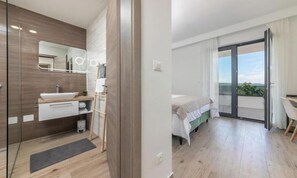Ein modernes Badezimmer mit einem großen Spiegel, einem Waschbecken und einer Duschkabine. Der Raum hat einen Holzboden und ein Bett mit Blick ins Freie.