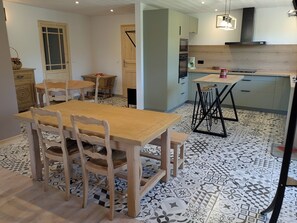 A dining area with a wooden table and chairs, a kitchen with a stove and sink, and patterned floor tiles. - Large T4 garden apartment in a renovated farmhouse in a peaceful village. (Mieussy)