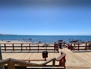 A wooden deck with a railing overlooking a beach with rocks and the sea. - Beachfront 2BR scenic sea views - Pool (Mijas)