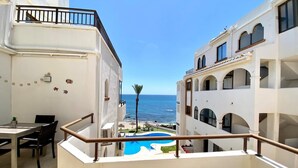 A balcony with a view of the sea, a pool, and a dining area with chairs and a table. - Beachfront 2BR scenic sea views - Pool (Mijas)