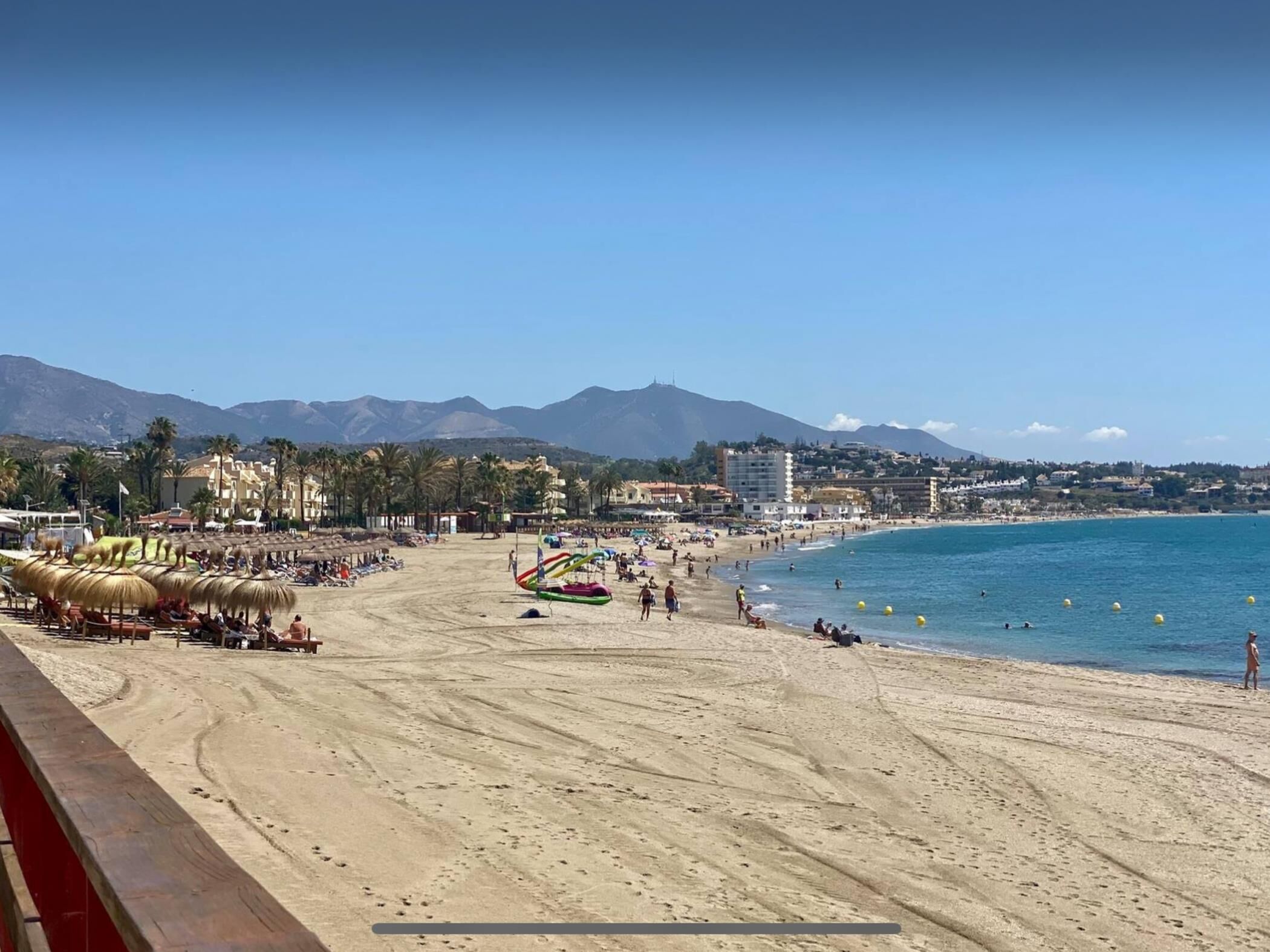 Una playa con sombrillas, una torre de salvavidas y una vista despejada del mar y las montañas.