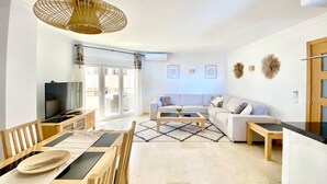 A modern living room with a dining area, a sofa, a coffee table, and a television. - Beachfront 2BR scenic sea views - Pool (Mijas)