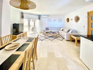 A modern living room with a dining area, a sofa, a coffee table, and a television. - Beachfront 2BR scenic sea views - Pool (Mijas)