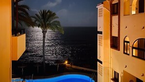 A night view of a building with a pool, a palm tree, and a view of the ocean. - Beachfront 2BR scenic sea views - Pool (Mijas)