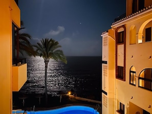 A night view of a building with a pool, a palm tree, and a view of the ocean. - Beachfront 2BR scenic sea views - Pool (Mijas)