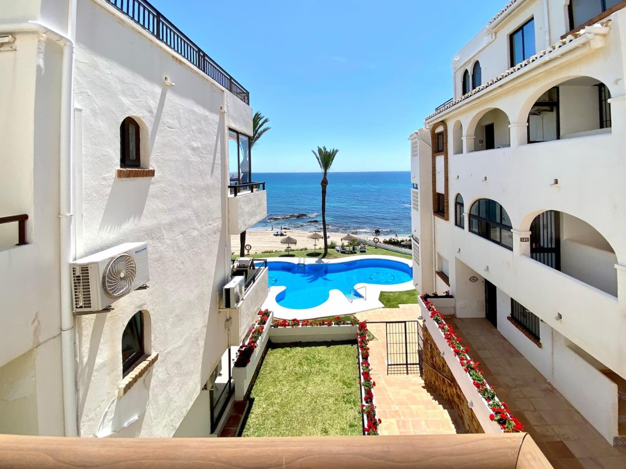 A hotel courtyard with a swimming pool, a view of the sea, and a palm tree.