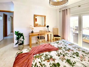 A bedroom with a bed, a desk, two chairs, a mirror, a potted plant, and a balcony view. - Beachfront 2BR scenic sea views - Pool (Mijas)