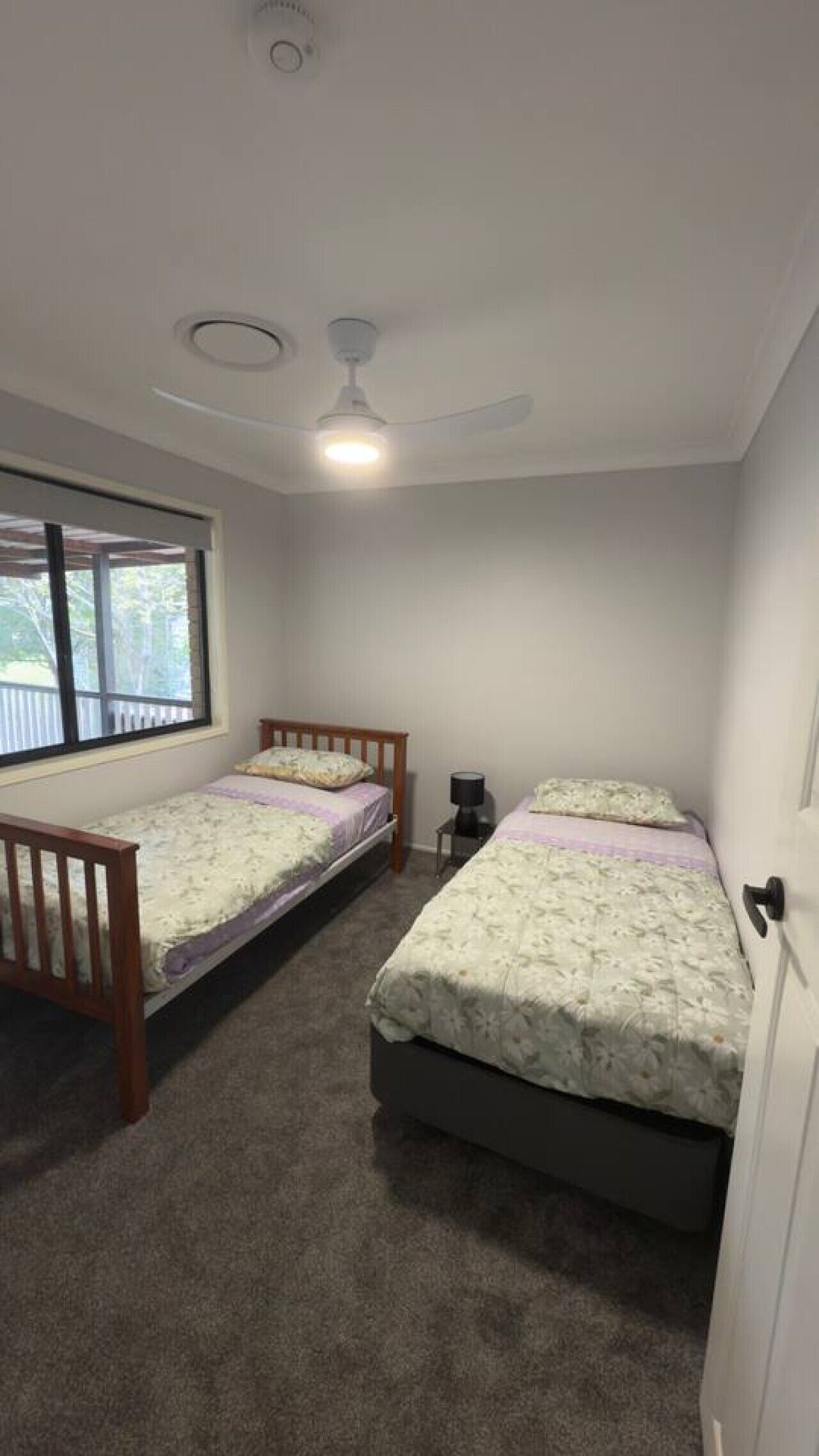 Ein Schlafzimmer mit zwei Einzelbetten, einem Deckenventilator, einem Fenster und einer Tür.