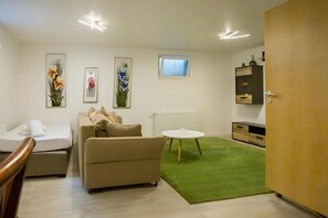 A modern living room with a sofa, a small table, a green rug, and a TV on the wall. - Business Apartment Kaiserslautern · Sleeps 2 · Full Kitchen · Living Room (Kaiserslautern)