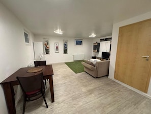 A room with a dining table, chairs, a sofa, a television, and a wooden door. - Business Apartment Kaiserslautern · Sleeps 2 · Full Kitchen · Living Room (Kaiserslautern)