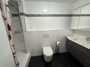 A bathroom with a toilet, a sink, a shower, and a mirror. - Business Apartment Kaiserslautern · Sleeps 2 · Full Kitchen · Living Room (Kaiserslautern)