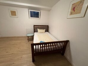 A bedroom with a wooden bed, a small table, a radiator, and two framed pictures on the wall. - Business Apartment Kaiserslautern · Sleeps 2 · Full Kitchen · Living Room (Kaiserslautern)
