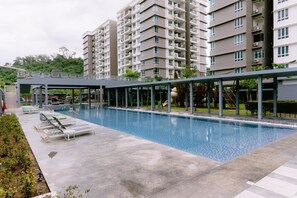 A swimming pool with lounge chairs, a covered walkway, and high-rise residential buildings in the background. - Trival Misty Cottage Homestay @ Sri Indah Sandakan (Sandakan)