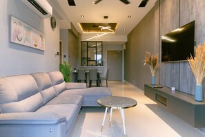 A modern living room with a sectional sofa, a round coffee table, a dining area with chairs, a flat-screen TV, and a wall-mounted air conditioner. - Trival Misty Cottage Homestay @ Sri Indah Sandakan (Sandakan)