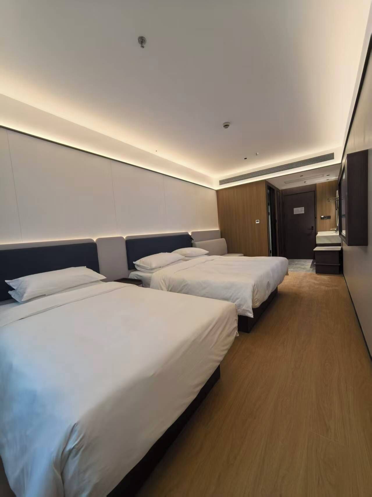 Habitación de hotel con tres camas, piso de madera, una puerta y un pequeño escritorio con espejo.