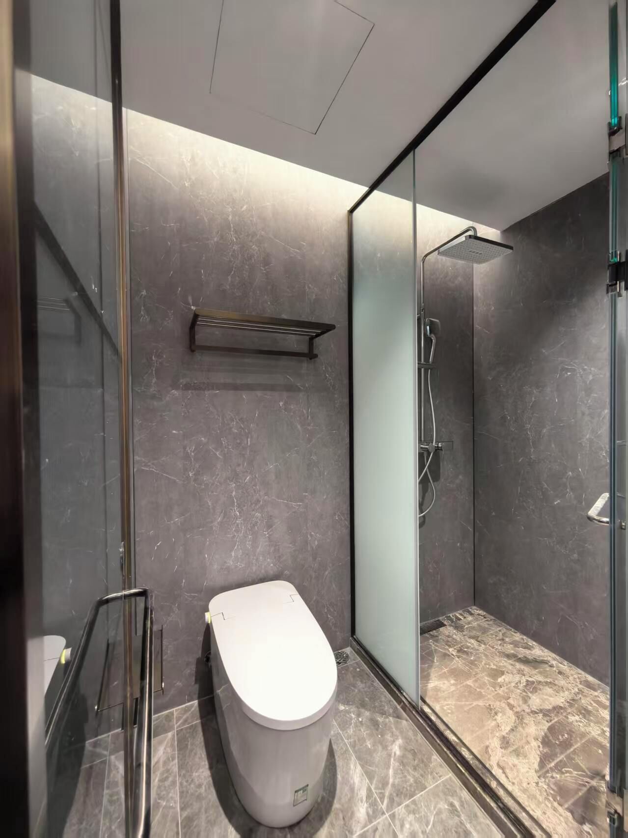 A modern bathroom with a glass-enclosed shower, a toilet, and a marble-tiled floor.