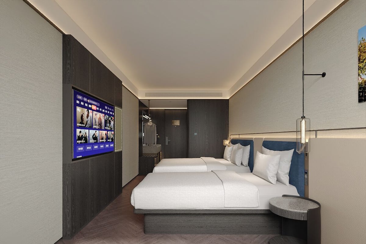 A modern hotel room with a large bed, a small bedside table, a wall-mounted TV, and a separate bathroom area.