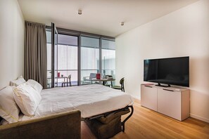 Ein Hotelzimmer mit einem Bett, einem Fernseher, einem Esstisch mit Stühlen und großen Fenstern.