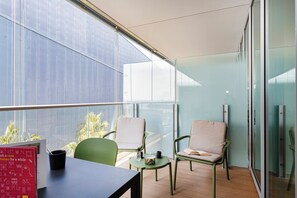Ein Balkon mit zwei Stühlen, einem Tisch und einer Glastrennwand.