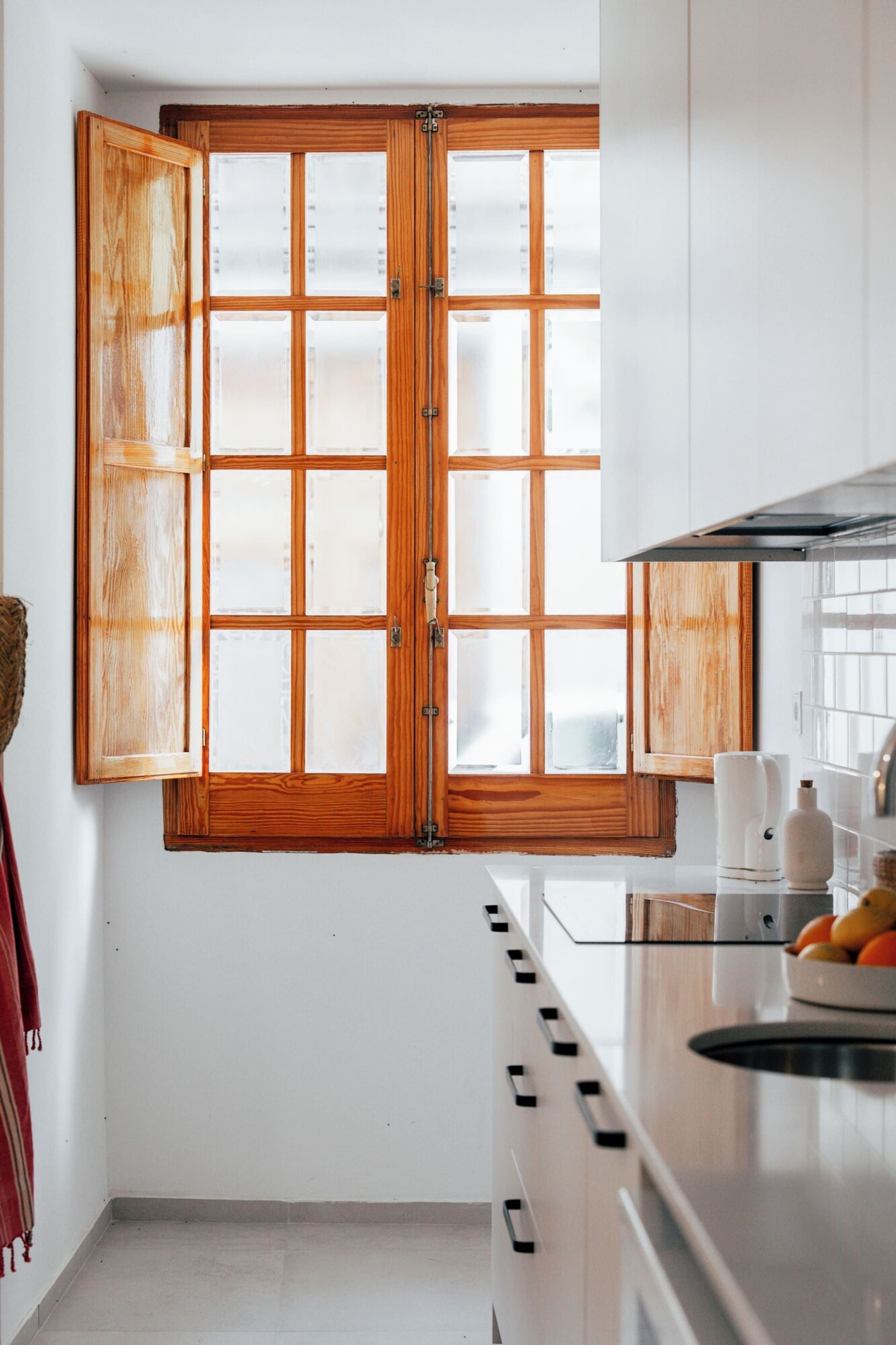 Une cuisine dotée d’une grande fenêtre à cadre en bois, de meubles blancs et d’une hotte de cuisinière en acier inoxydable.