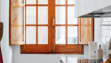 Une cuisine dotée d’une grande fenêtre à cadre en bois, de meubles blancs et d’une hotte de cuisinière en acier inoxydable.