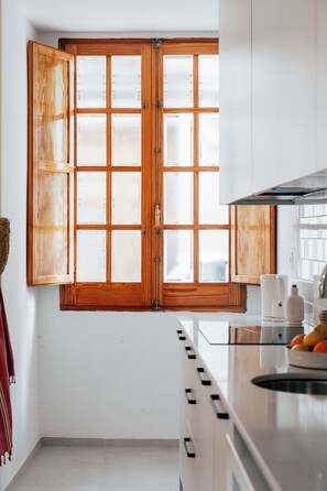 A kitchen with a large wooden-framed window, white cabinets, and a stainless steel range hood.