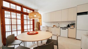 A modern kitchen with white cabinets, a round dining table with chairs, and a large window with wooden frames. - Two-bedroom apartment (Picaña)