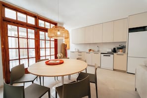 Een moderne keuken met witte kasten, een ronde eettafel met stoelen en een groot raam met houten kozijnen.