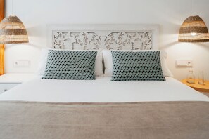 A bed with a white headboard and two patterned pillows, two wall-mounted lamps, and a bedside table with a glass container and a bottle.