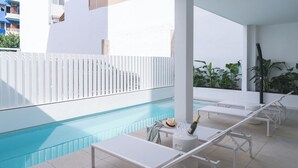 A poolside area with lounge chairs, a small table with a bottle and glass, and a white fence. - Two-bedroom apartment (Picaña)